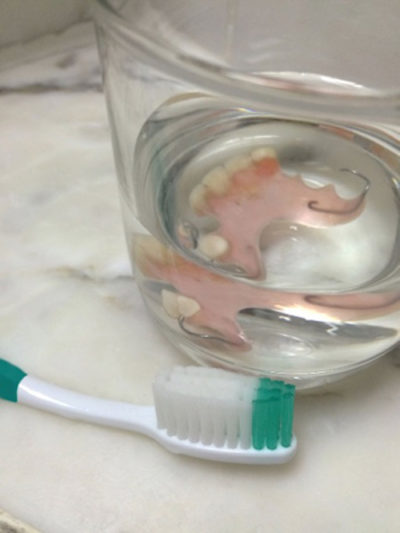 Affordable partial dentures placed inside a glass of cleaning solution